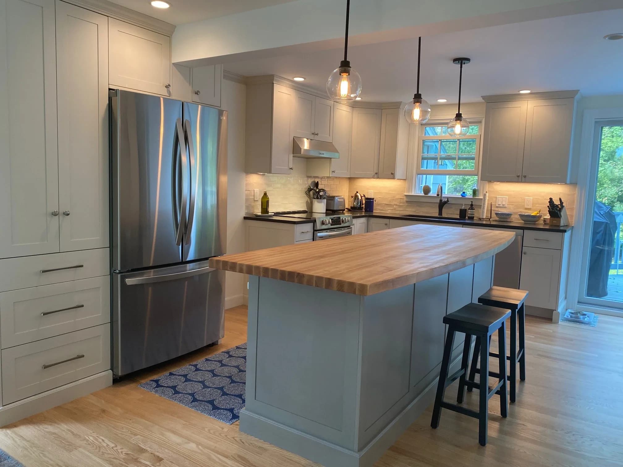 Concord NH kitchen — light gray shaker cabinets, butcher block island with bar seating, black stone counters